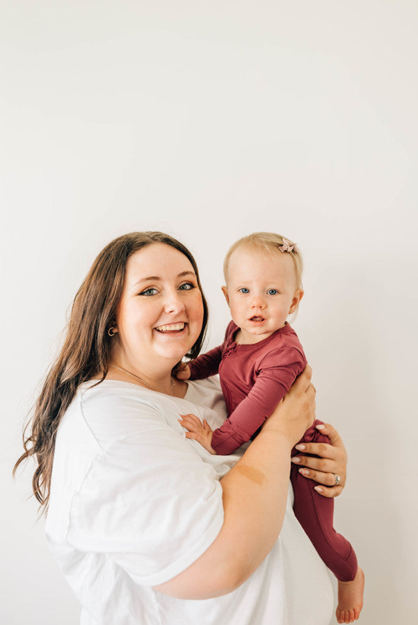 Baby Wearing Luna Luz Two-Way Zip Romper in Cranberry Held by Mother