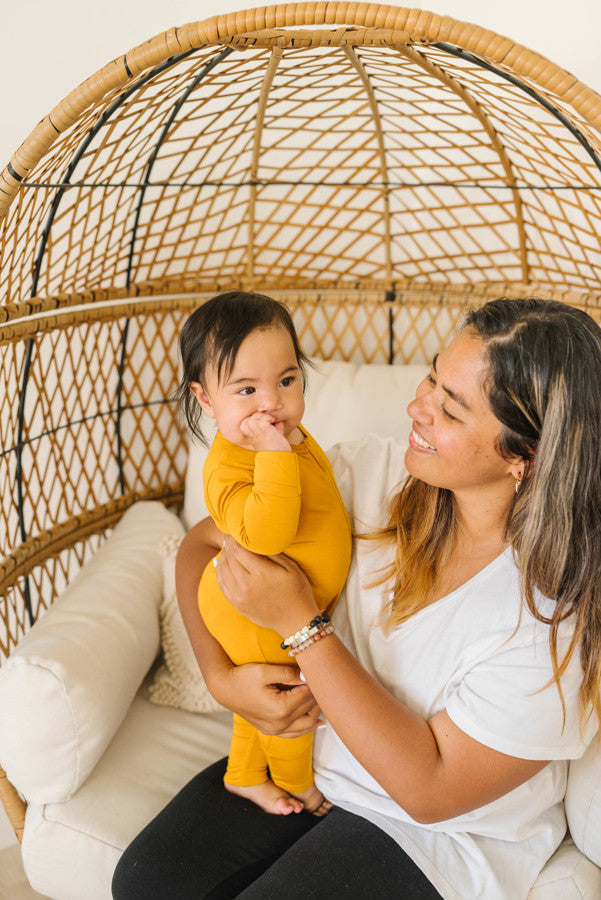 Baby Wearing Luna Luz Two-Way Zip Romper Pajama in Mustard Held by Mother