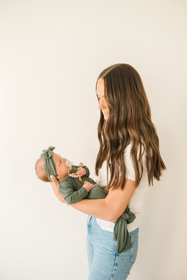 Baby Wearing Luna Luz Olive Bow Headband and Knotted Gown With Mother