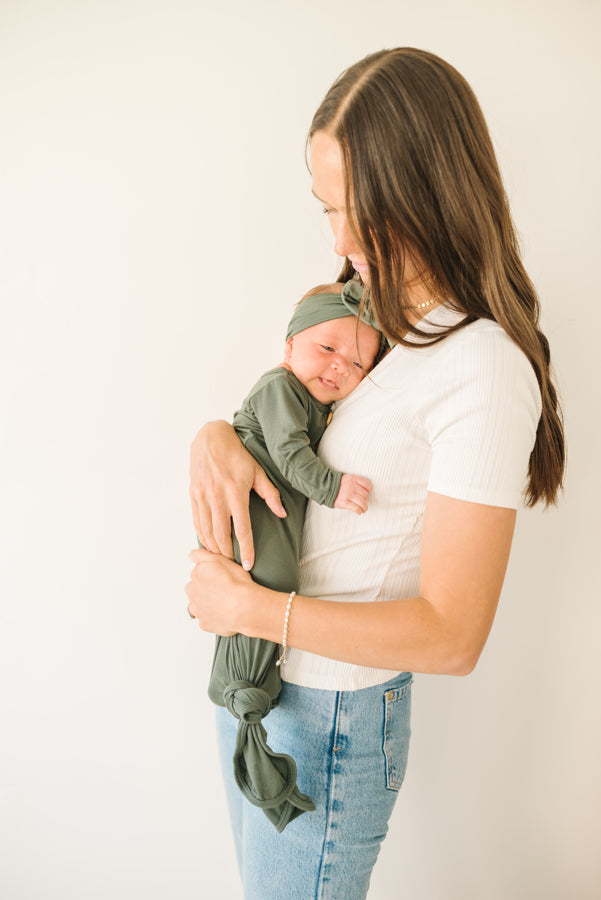 Baby Wearing Luna Luz Knotted Gown and Bow Headband in Olive Being Held by Mother